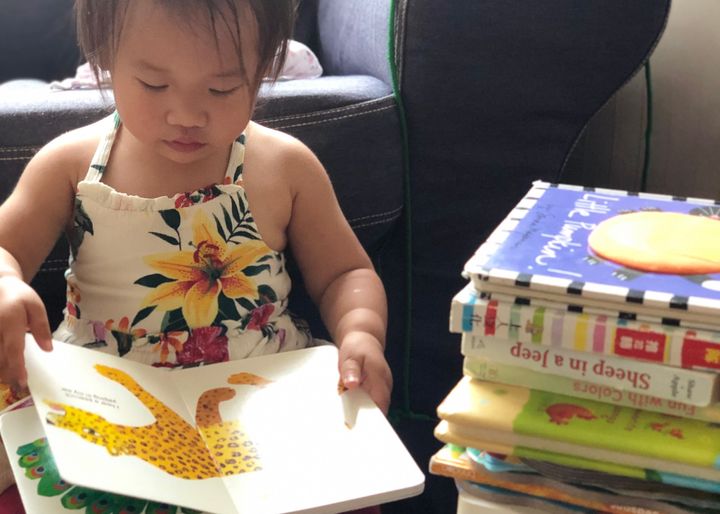 Toddler reading Eric Carle book next to stack of children's books